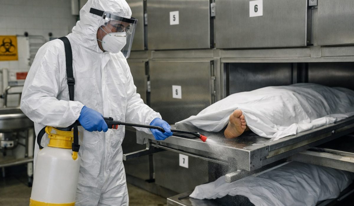 Agent de chambre mortuaire en tenue de protection désinfectant un chariot mortuaire pour prévenir les risques infectieux